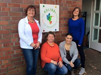 Team KOLIBRI: vier Frauen gruppiert um das Schild mit dem KOLIBRI-Logo